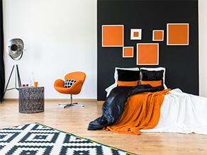 White and black wall with orange feature artwork and deco chair and blankets wooden floor and lamp